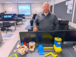 Richmond Community College student Robert Lewis stands with the two different parts of his CAD III project: a small engine and gear housing.